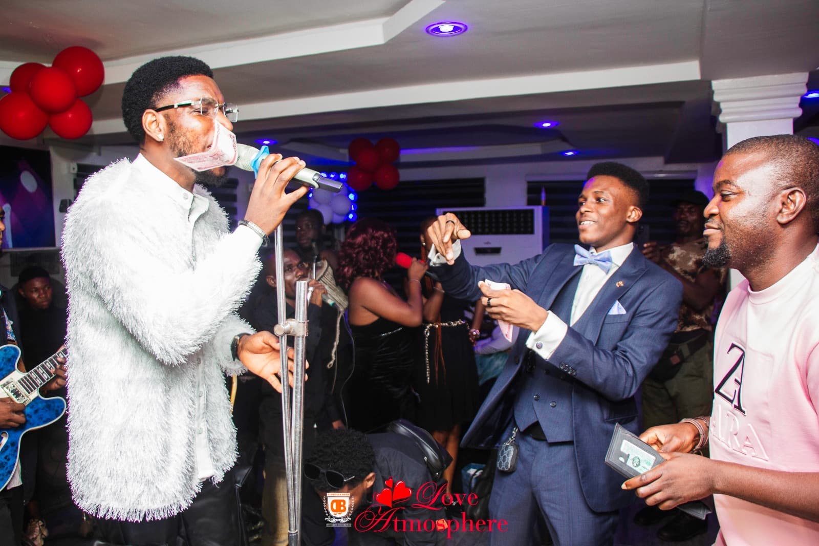 Singer in a white fuzzy jacket performs while a man in a suit sprays money.