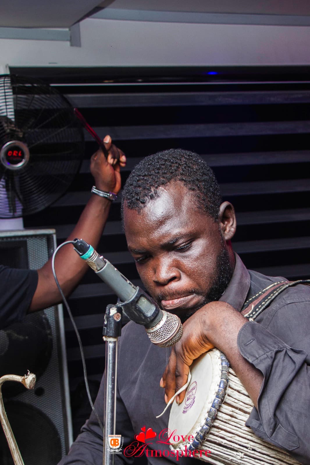 A focused musician playing a talking drum into a microphone during a live musical performance.