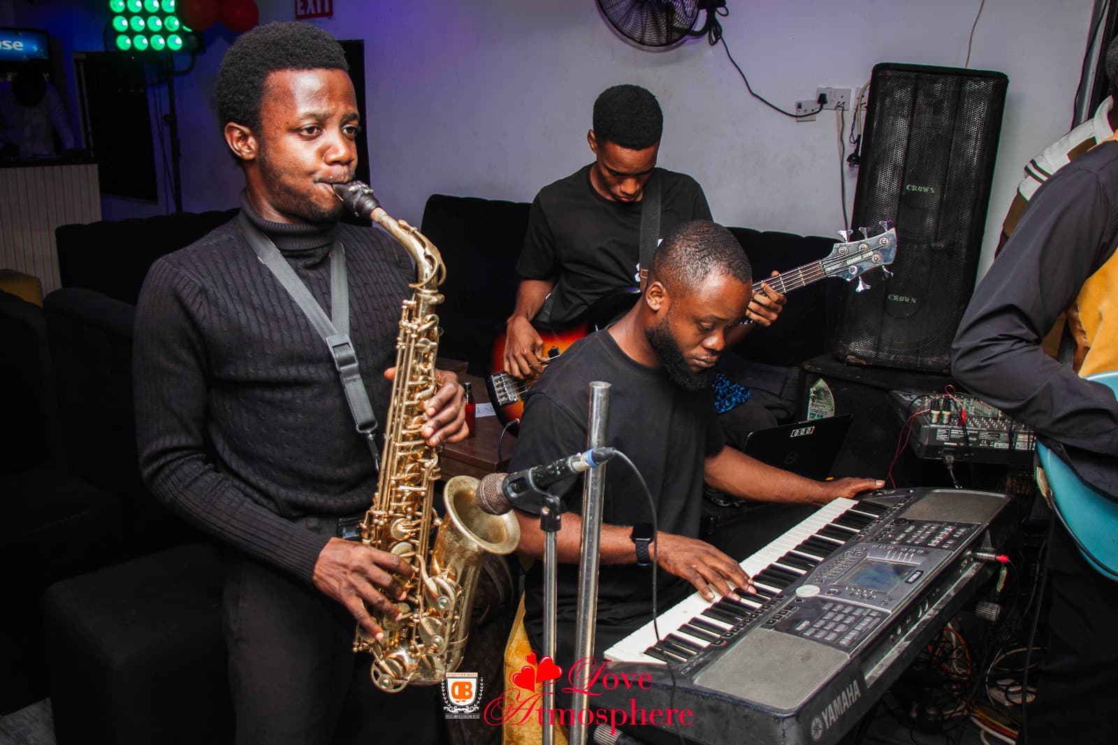 Three musicians performing live with a saxophone, keyboard, and bass guitar in a club.