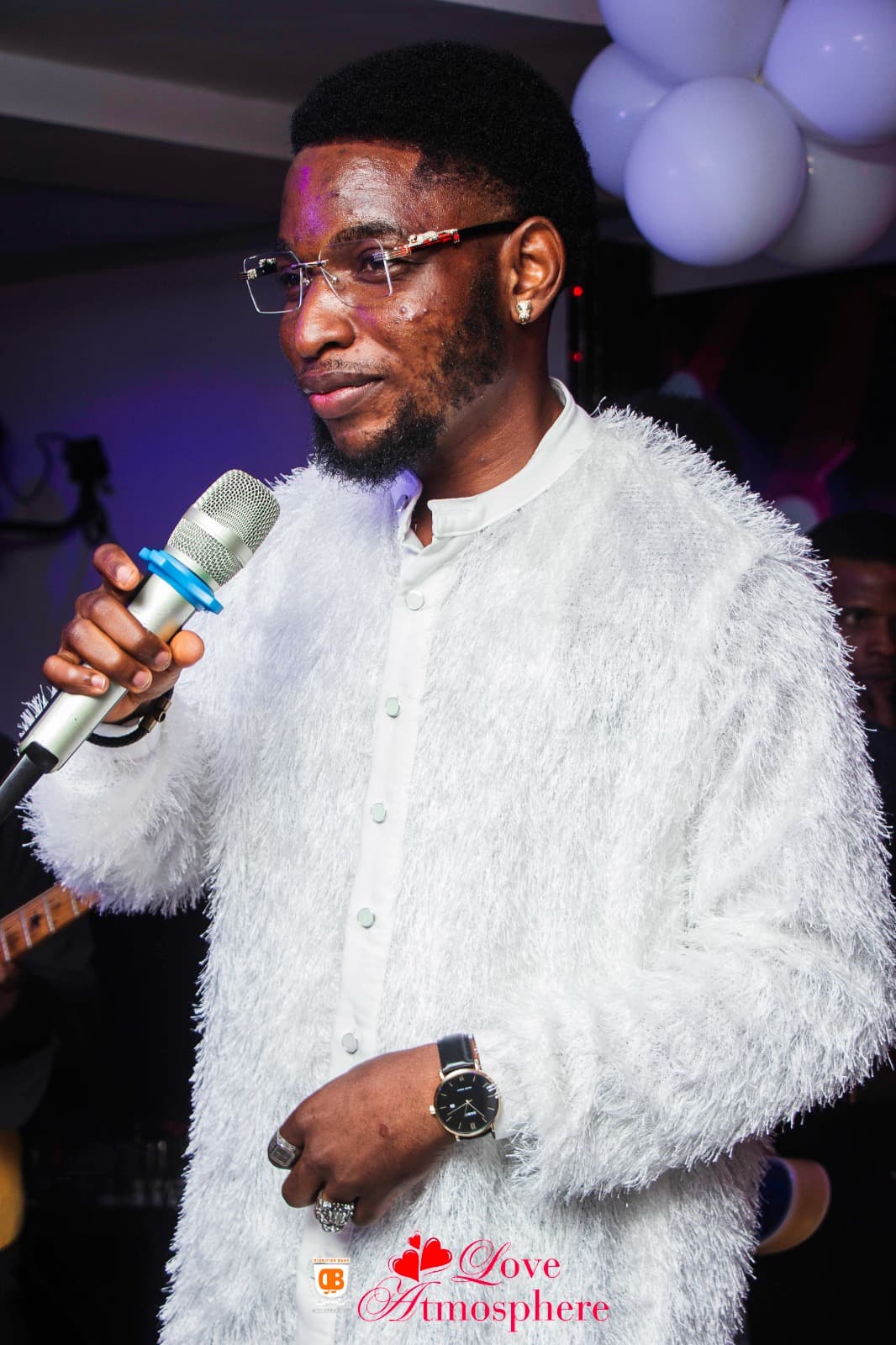Man with glasses and beard wearing a white textured jacket holding a microphone while performing.