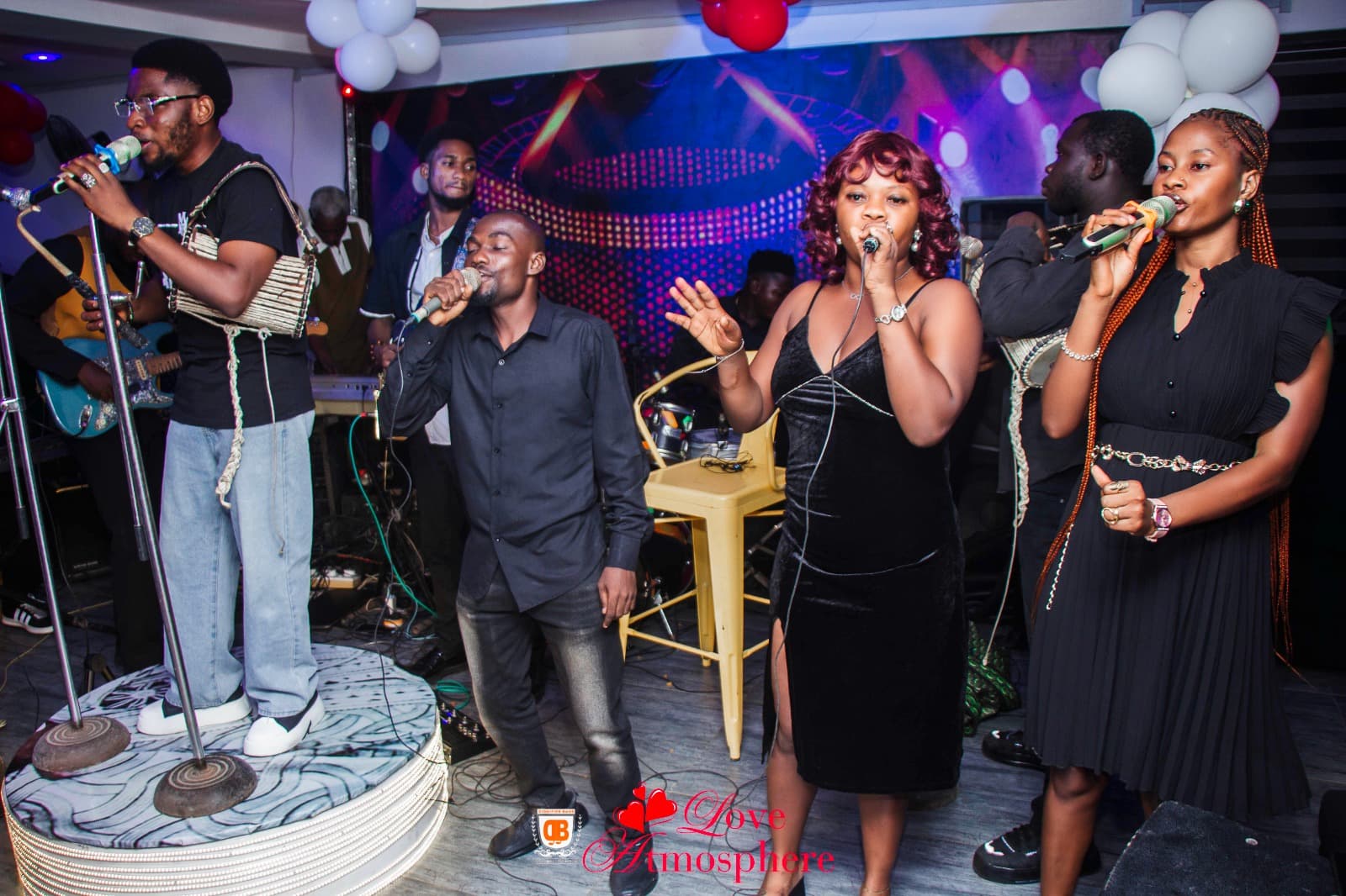 Diverse group of vocalists and musicians performing live on a stage with colorful lighting.
