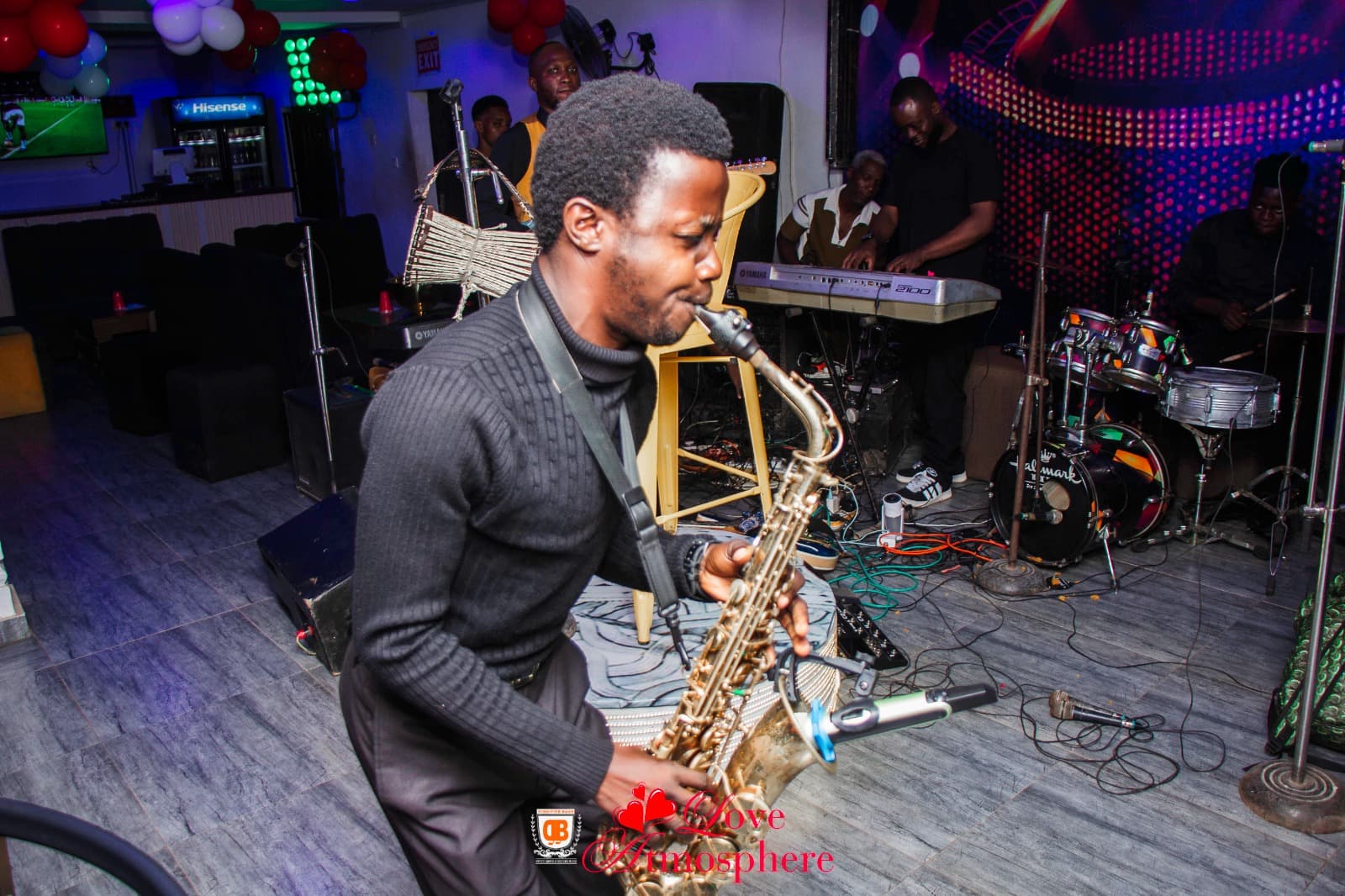 Saxophonist in a black turtleneck performs with a live band in a colorful nightclub.